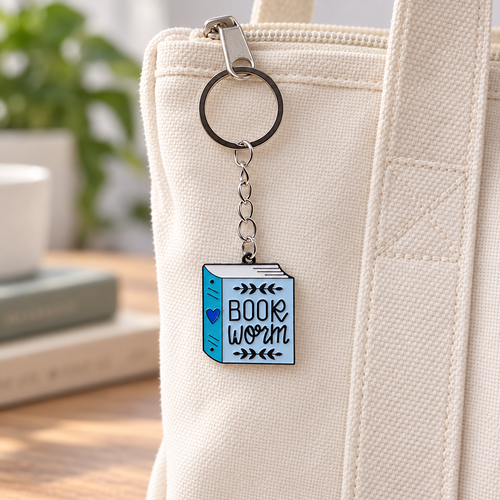 Blue Book Worm alloy charm and silver-tone keyring on a cream canvas tote; bag not included