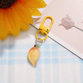 One curved golden-yellow fruit charm with a leaf detail and yellow clasp from the matching pair