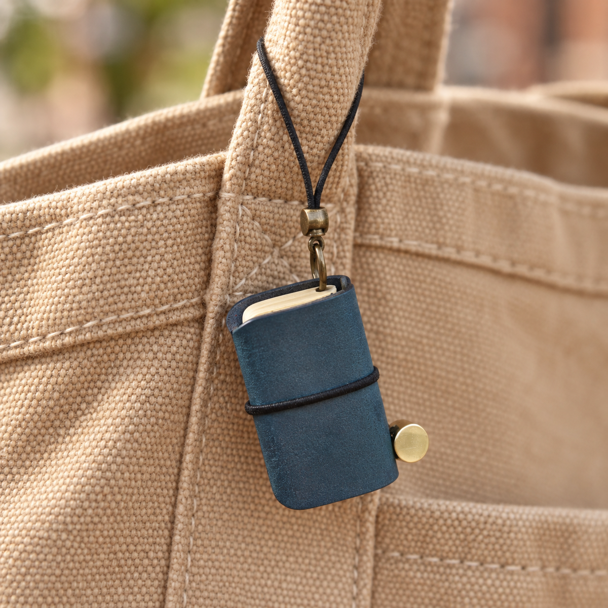 Ink-blue miniature notebook charm on a canvas bag; bag not included