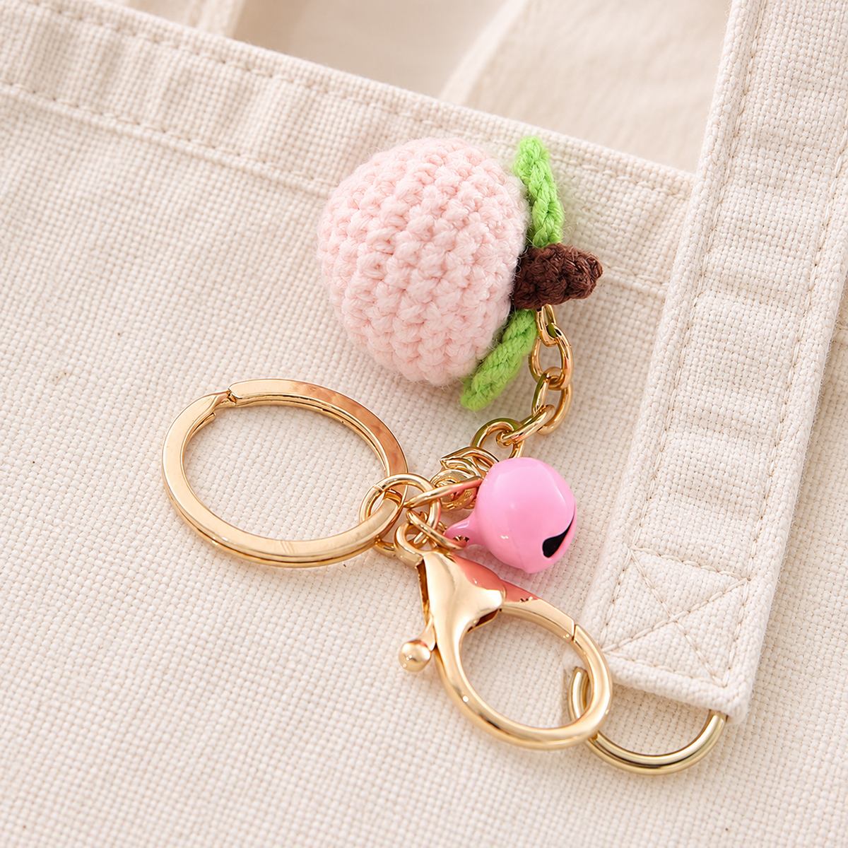 Crochet peach charm and pink bell styled on a cream tote; bag not included