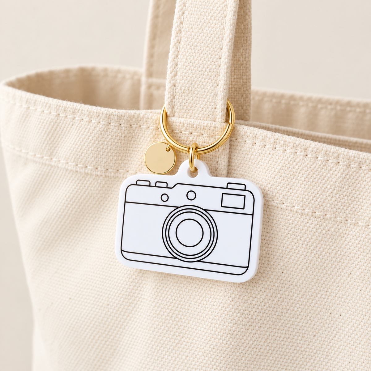 White camera-shaped acrylic charm attached to a neutral canvas tote