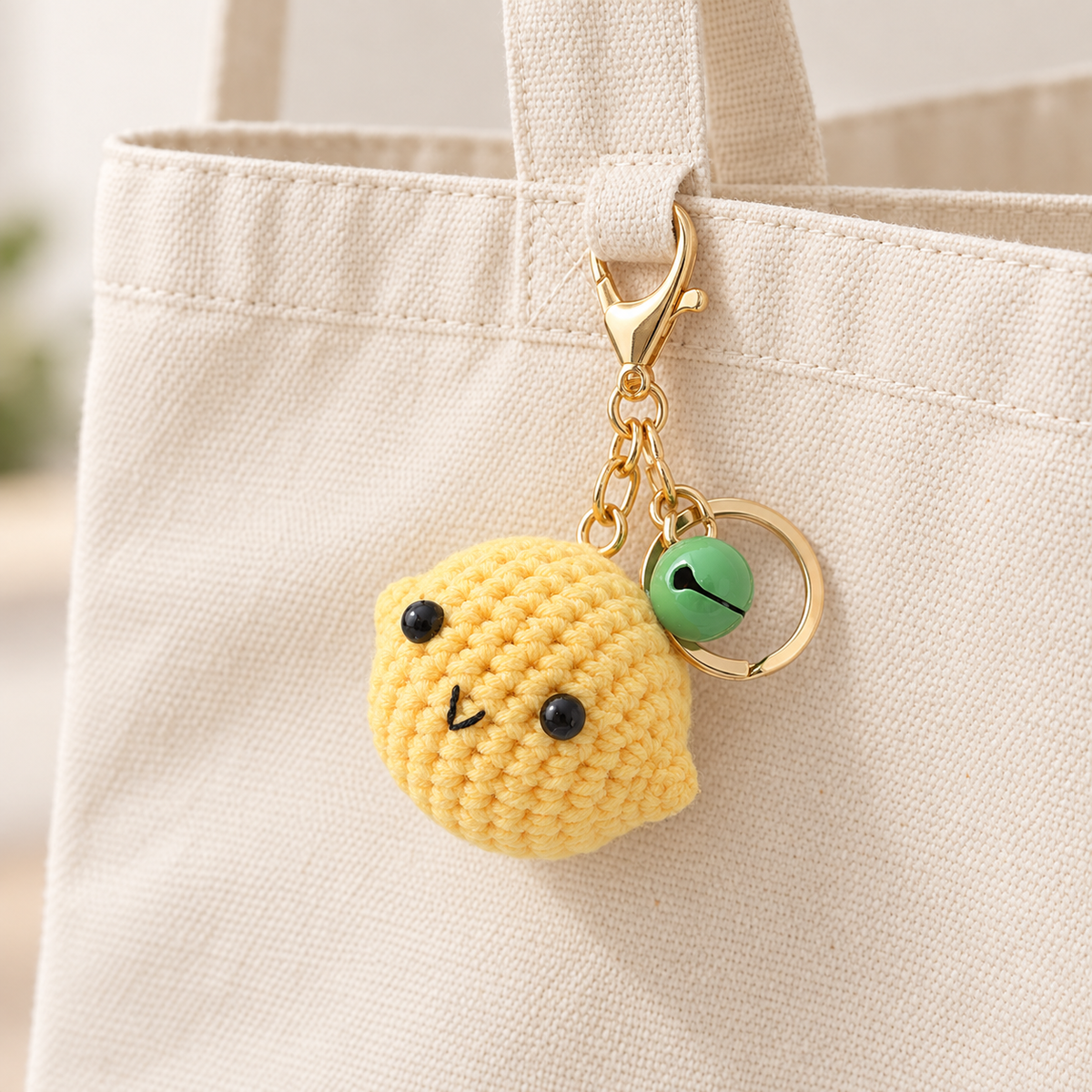 Crochet lemon charm with matching bell, clipped to a cream canvas tote; bag not included