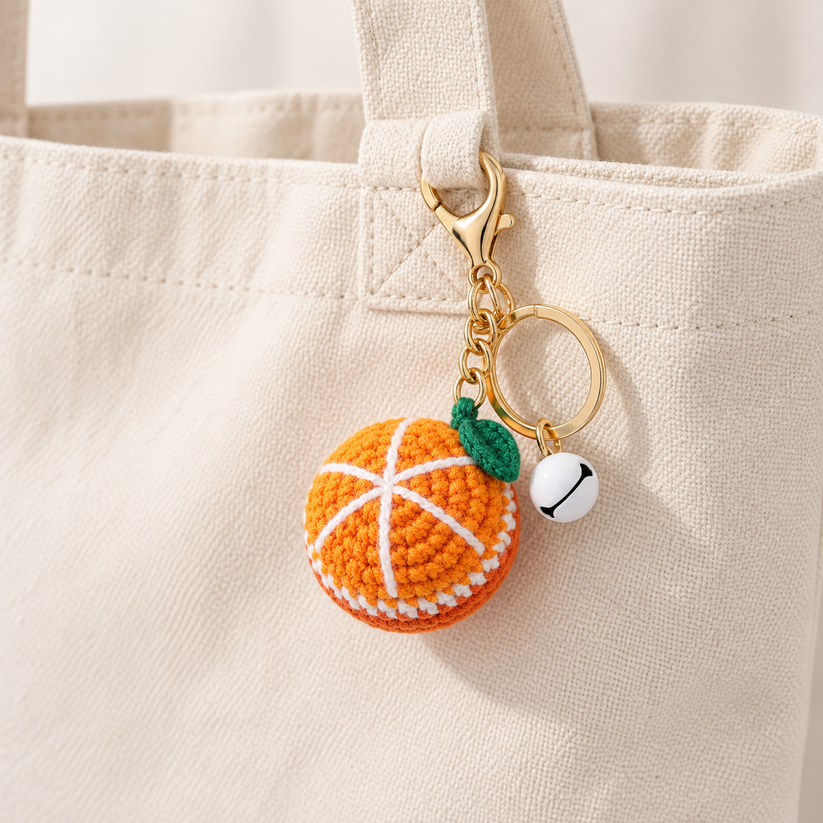 Crochet orange charm with matching bell, clipped to a cream canvas tote; bag not included