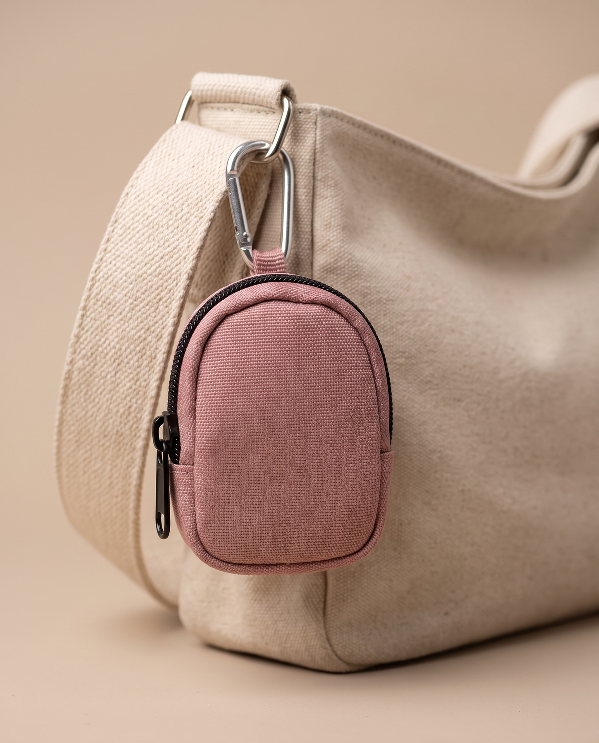 Dusty pink mini coin and earbud pouch charm on an oatmeal shoulder bag
