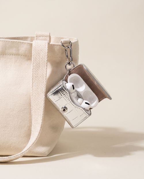 Black leather AirPods mini bag charm clipped to an ivory tote