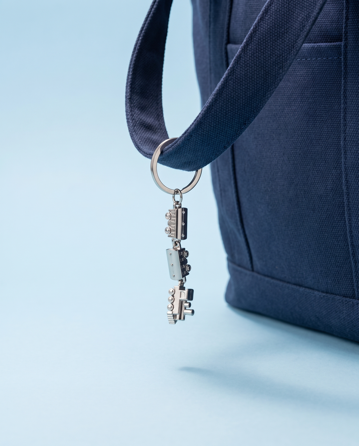 Mini silver train metal charm hanging from a navy canvas tote