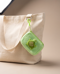Green plush turtle coin pouch charm clipped to a cream canvas tote