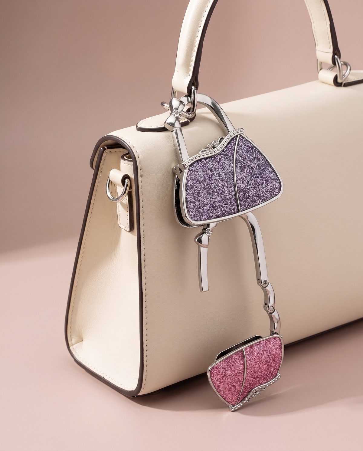 Mini handbag-shaped purse hook charm on an ivory handbag
