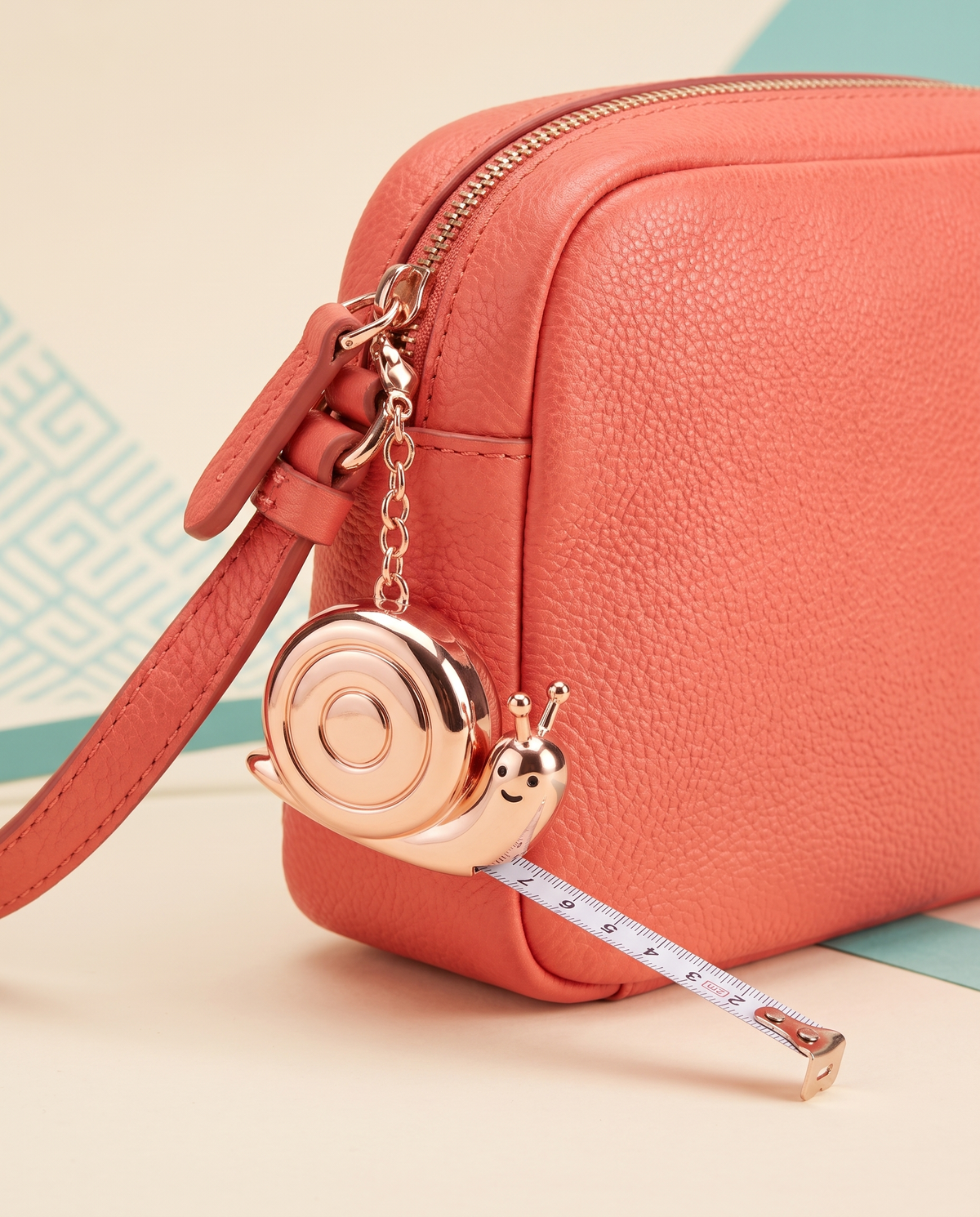 Mini snail tape measure charm on a coral crossbody bag