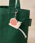 Snail measuring tape charm clipped to a forest green tote