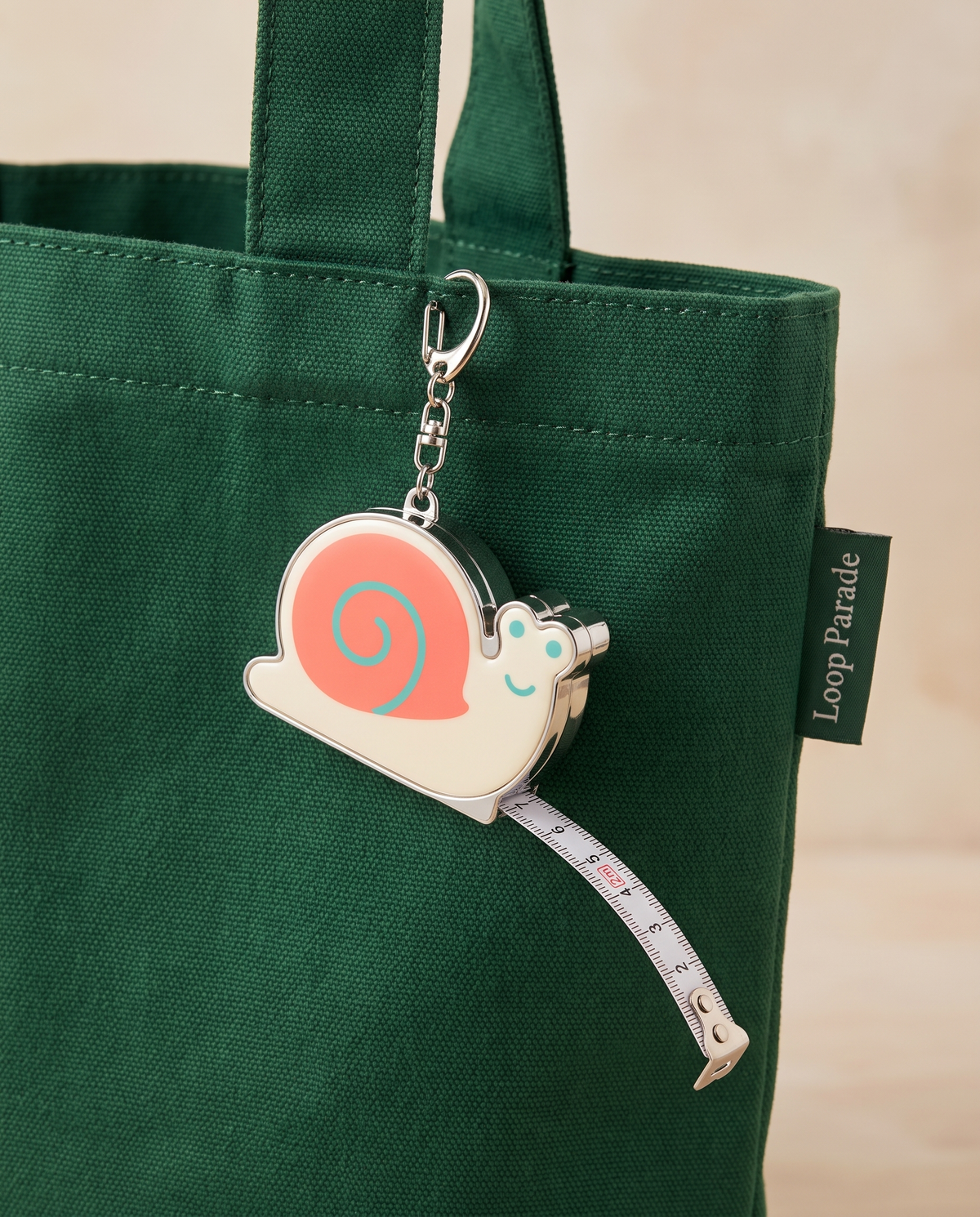 Snail measuring tape charm clipped to a forest green tote